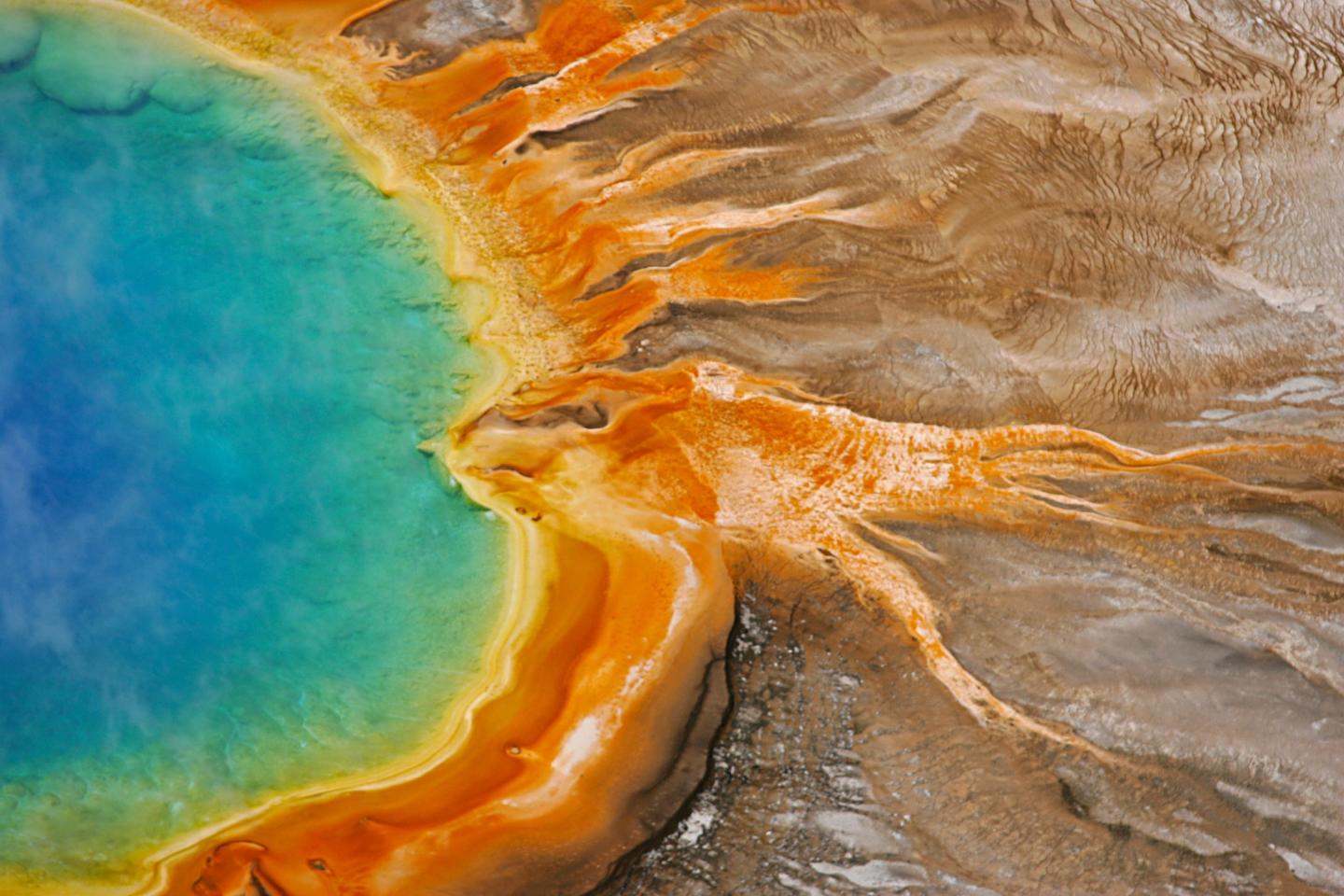 Colorful geothermal pool with vivid blue, yellow, and orange hues, surrounded by rocky terrain.