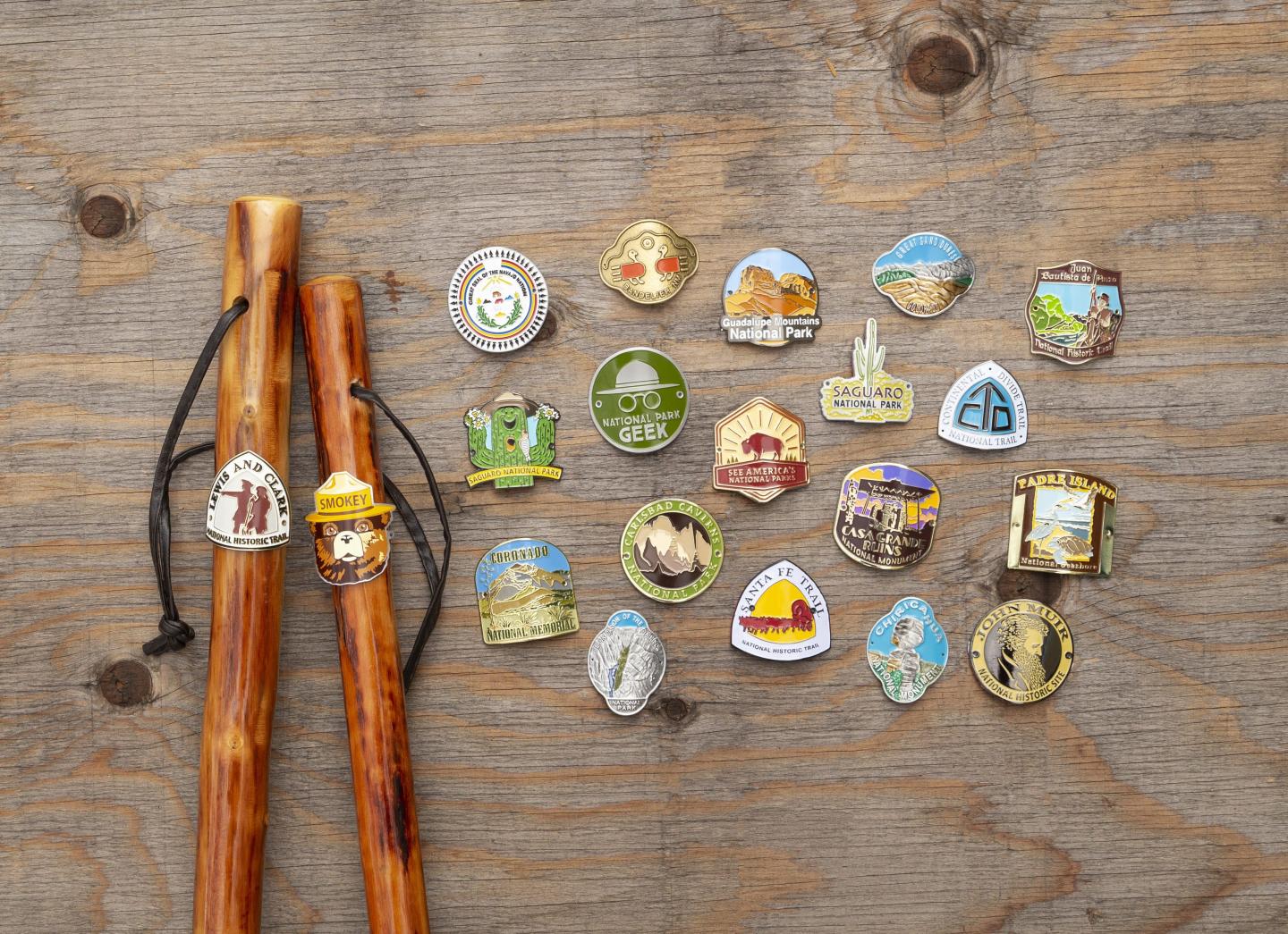 Walking sticks with colorful hiking badges on a wooden surface.