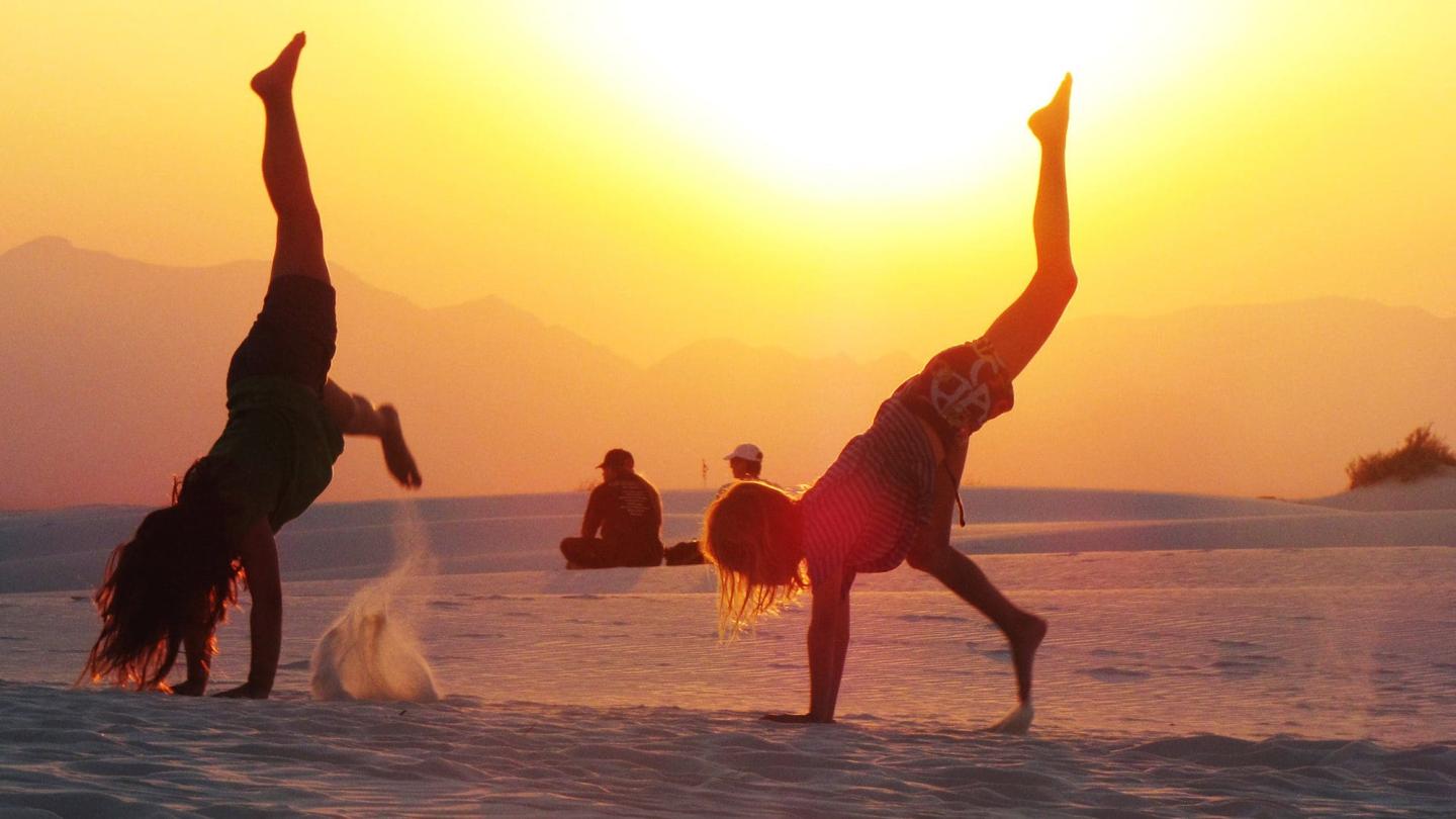 People doing cartwheels on a sandy beach at sunset.