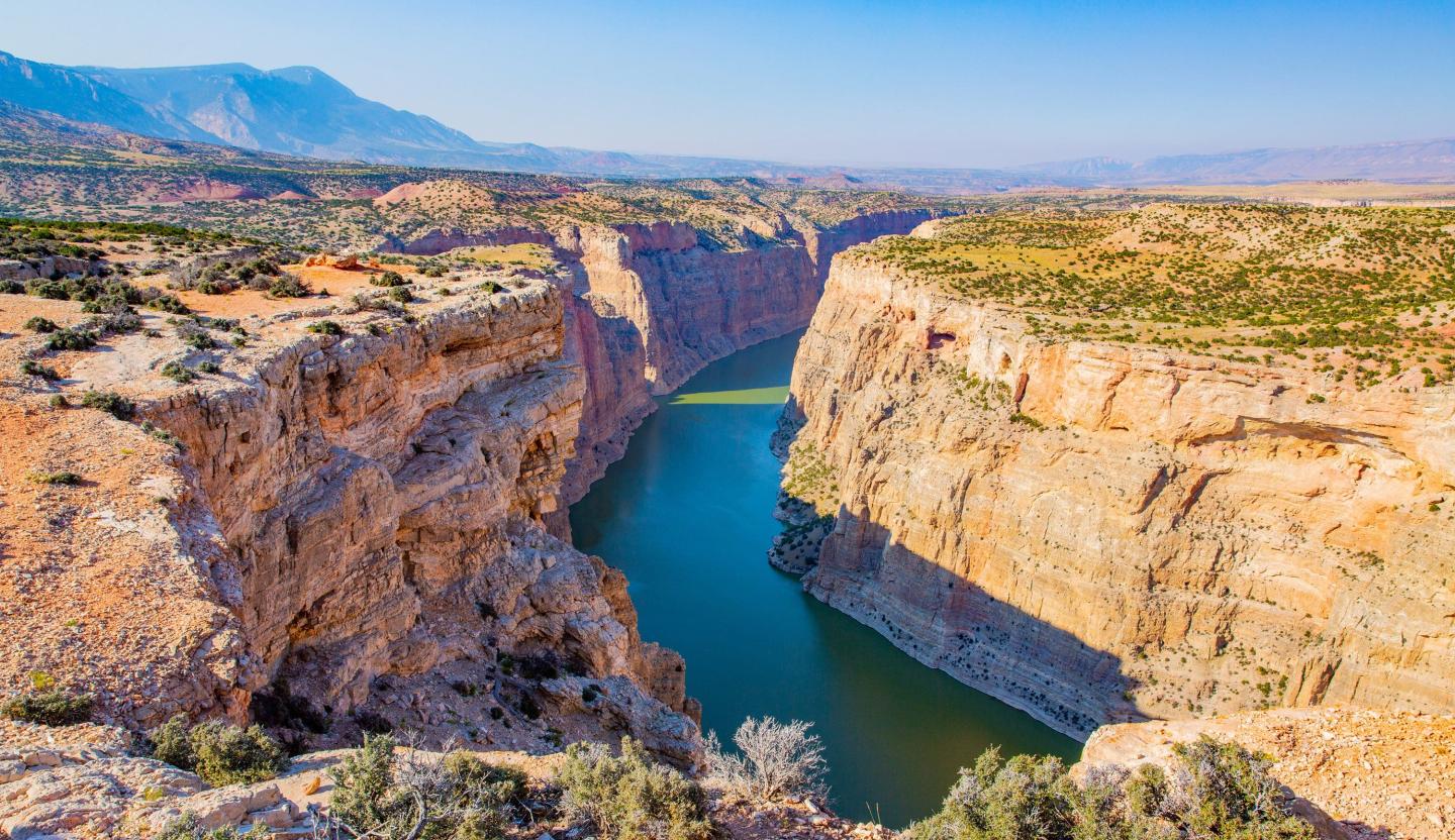 Canyon with a winding river, surrounded by rugged cliffs under a clear blue sky.