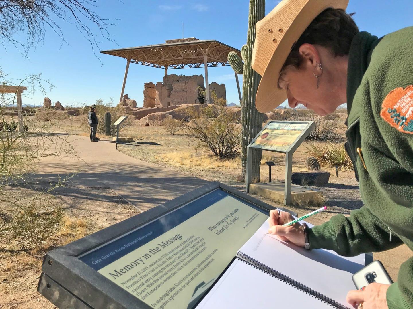 Park ranger writing notes in a desert landscape with historical ruins.