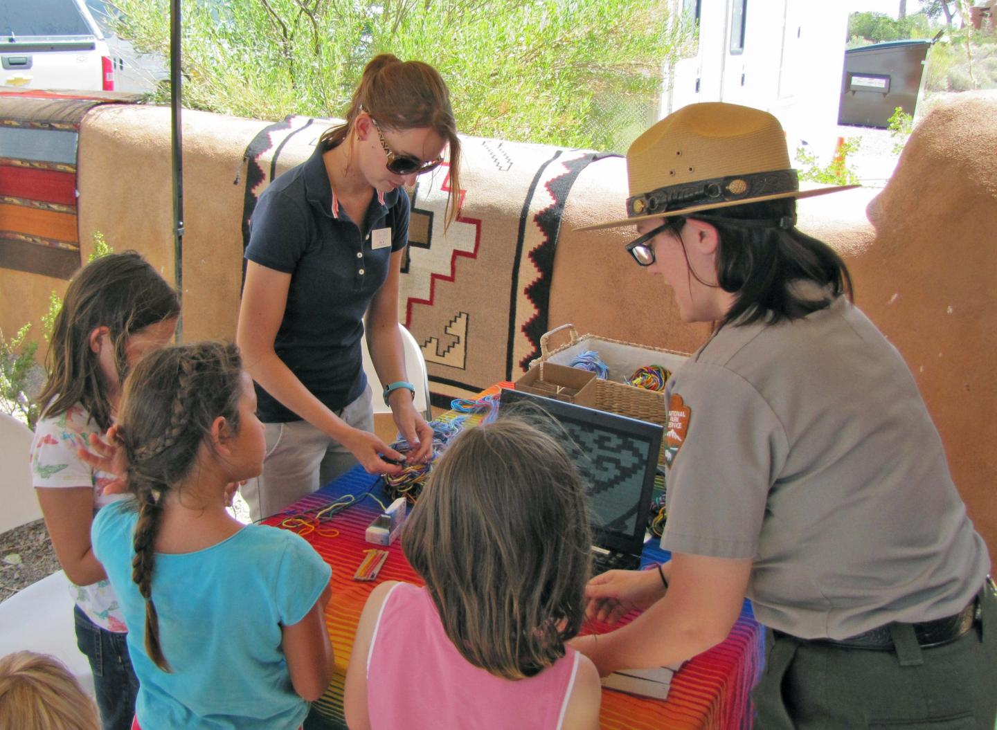 Kids interacting with two adults at a colorful outdoor table.
