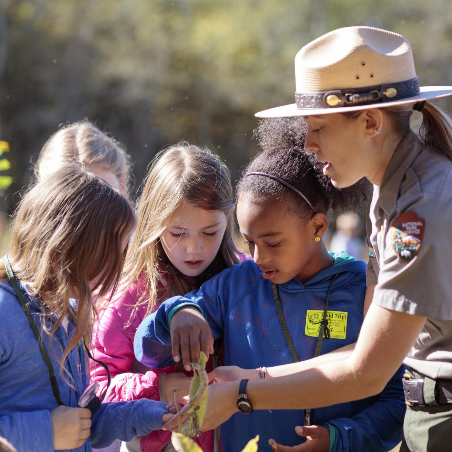 Park ranger showing children a leaf outdoors.