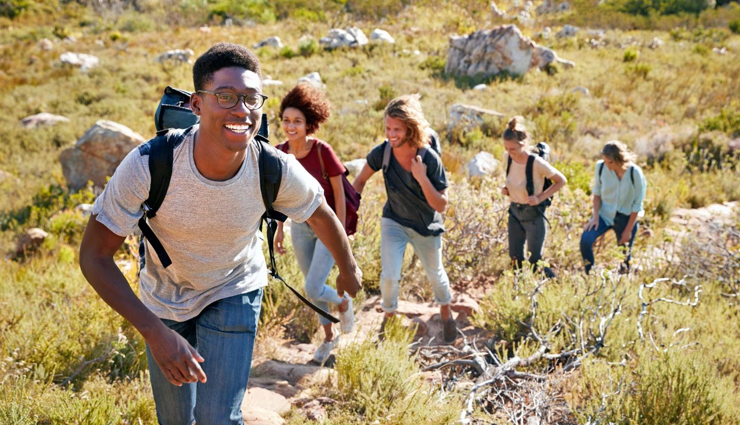 Group hiking up a sunny, grassy hillside, smiling and enjoying the outdoors.
