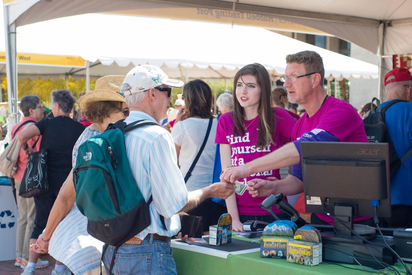 Booth staff assisting festival attendees under a tent.