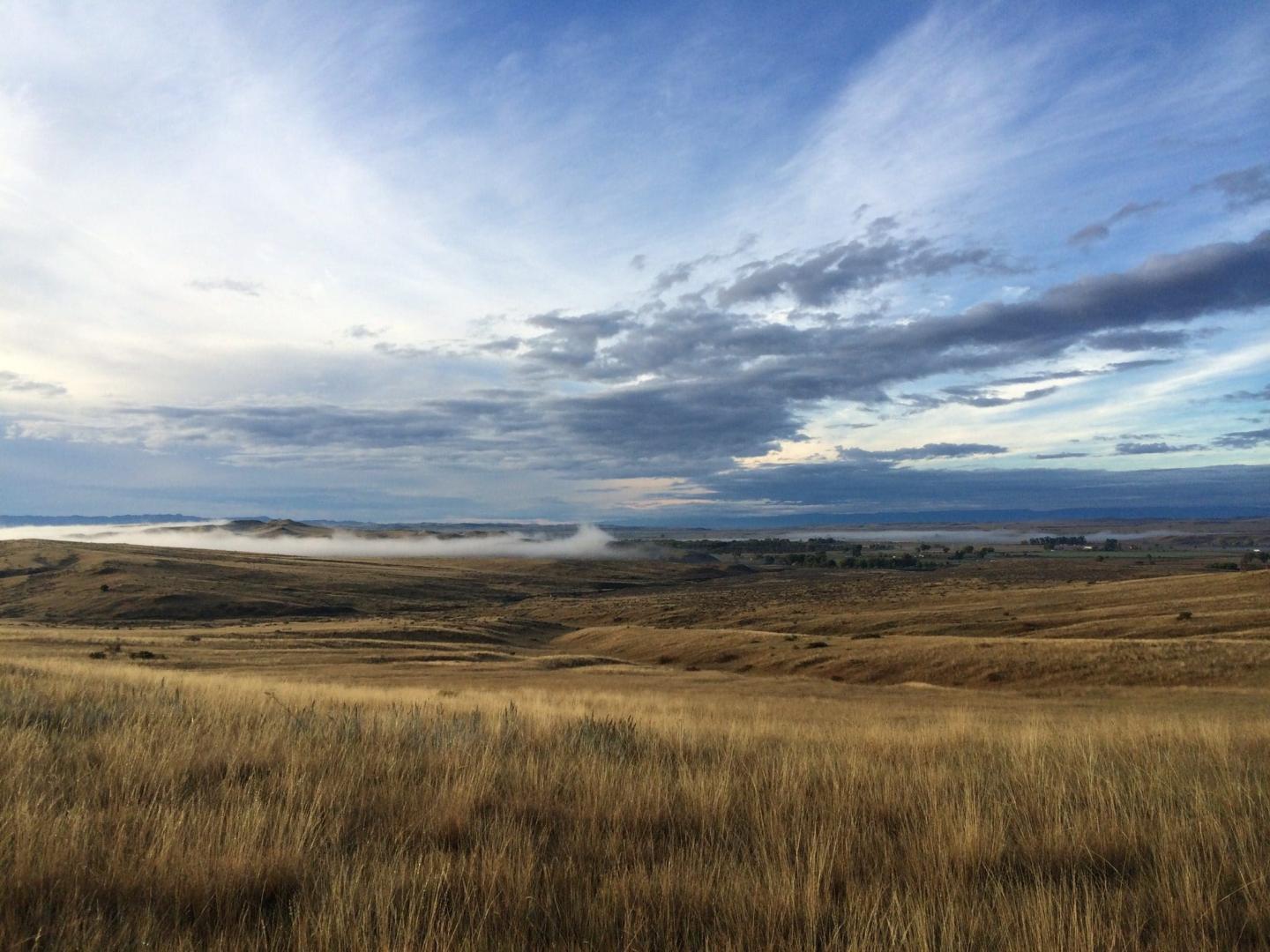 Open field landscape under vast blue sky with scattered clouds at Little Bighorn Battlefield .