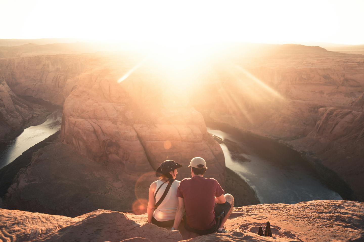 Two people sit on a cliff at sunset overlooking a winding river.