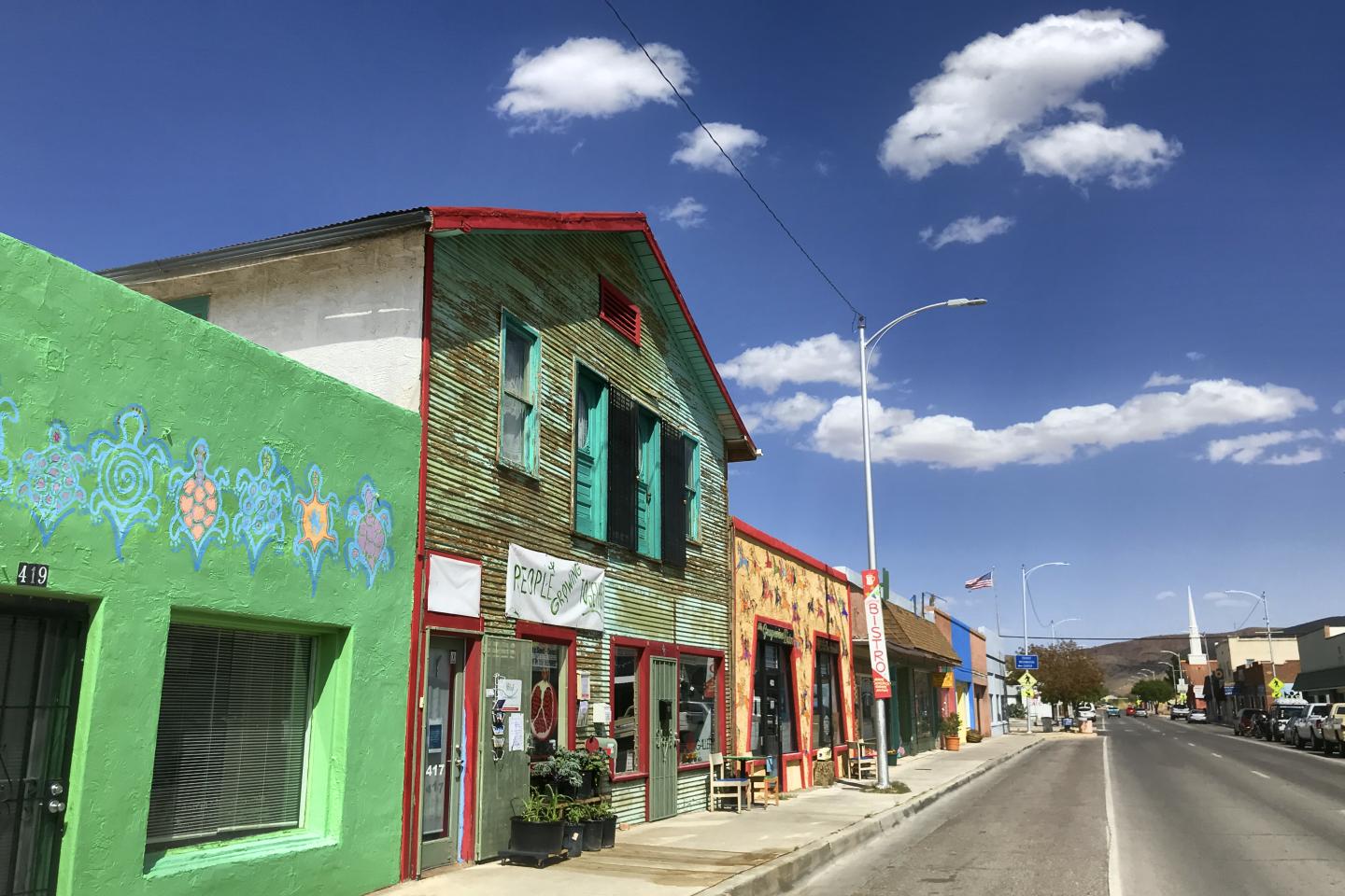 Colorful storefronts on a sunny street under a blue sky with clouds.