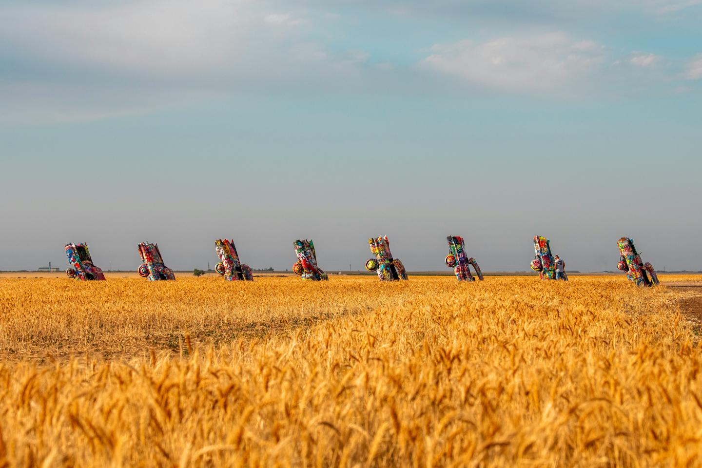 Cadillac sculptures half-buried in a golden wheat field under a blue sky.