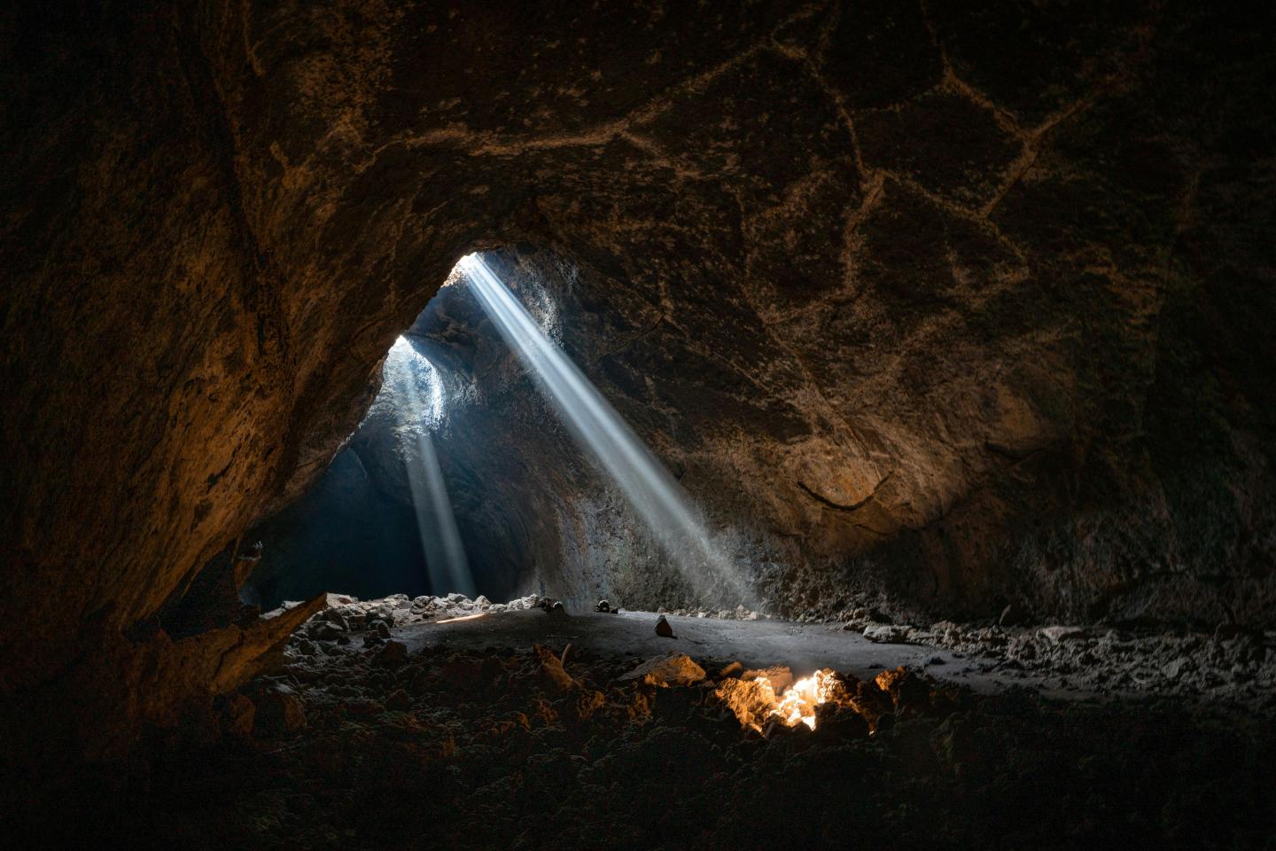 Sunlight beams through cave opening, illuminating the rocky ground.