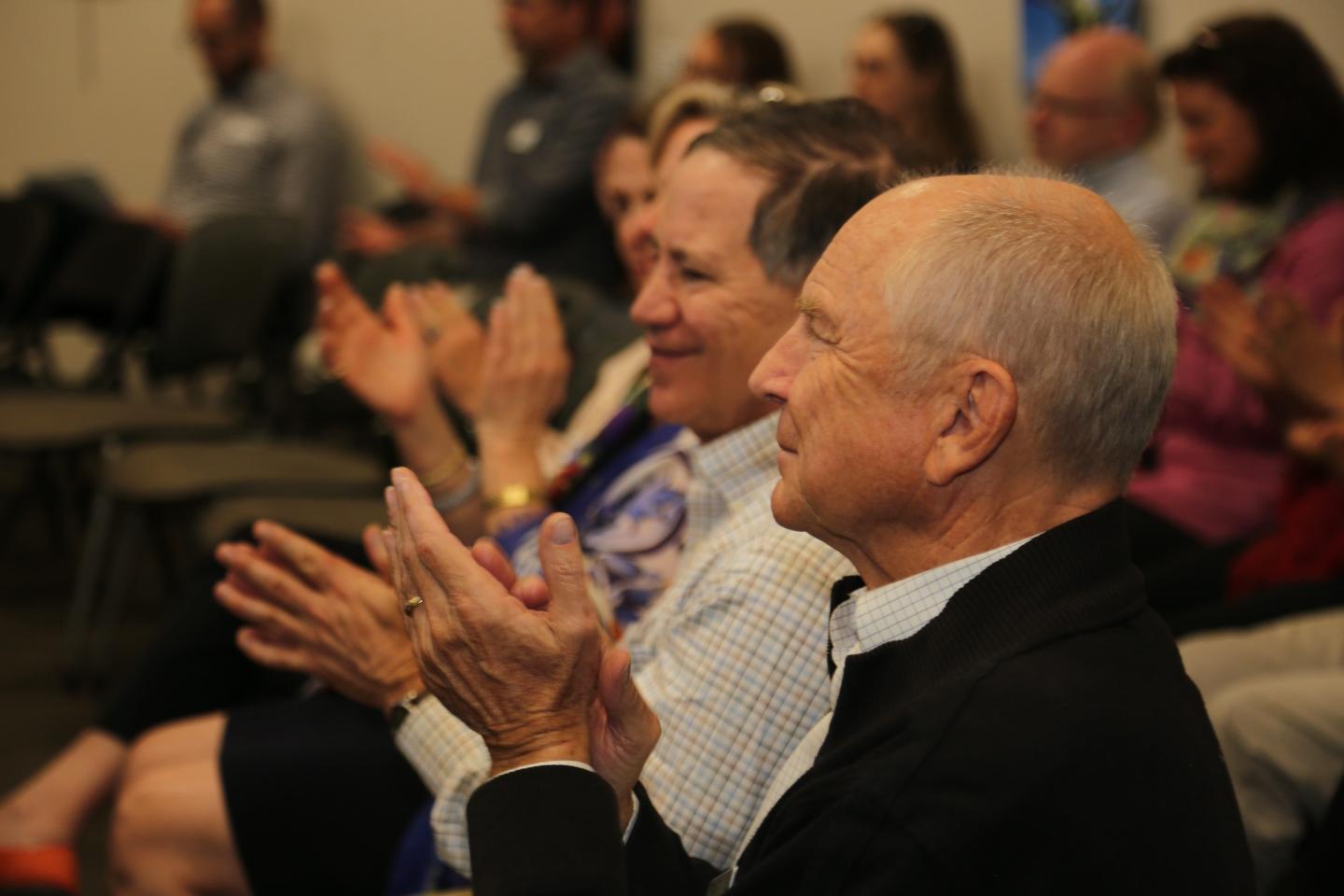 Audience clapping at an event, seated in rows, focused expressions.