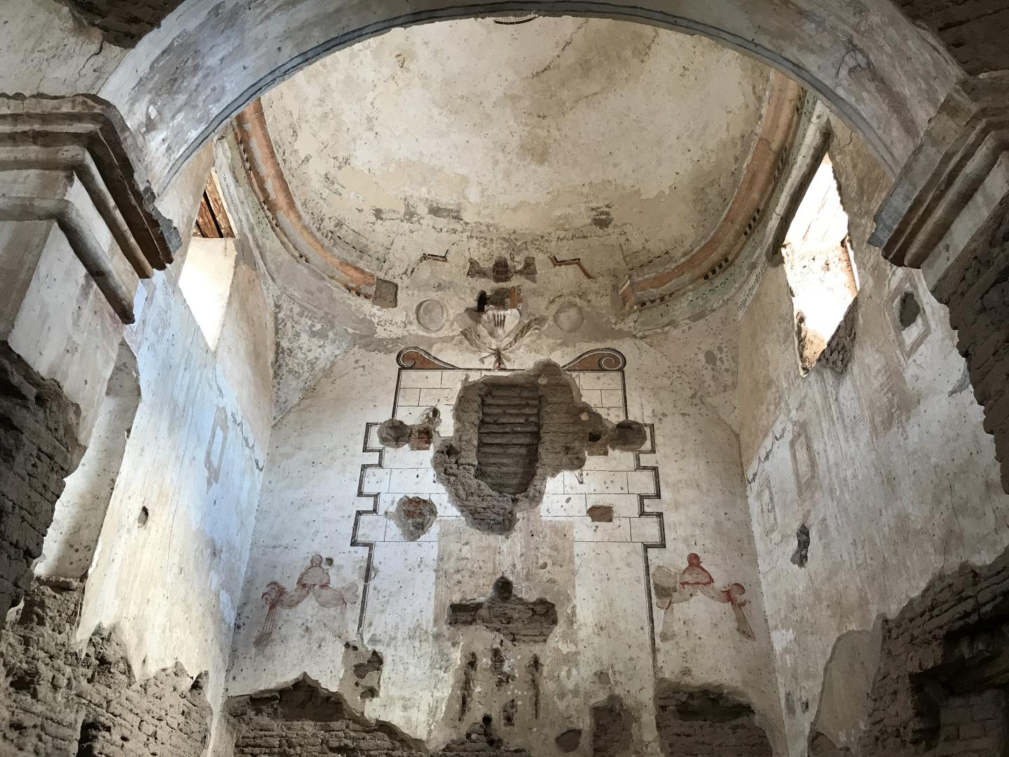 18th-century Franciscan mission church interior with faded mural and arched ceiling.