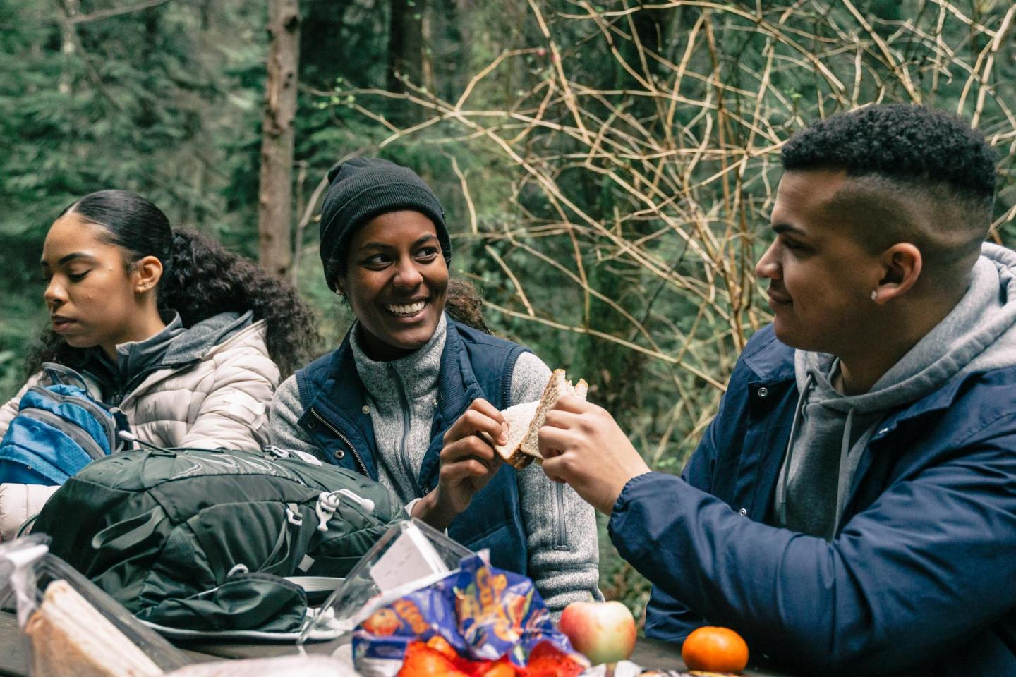 Three people enjoying a picnic outdoors, surrounded by trees.