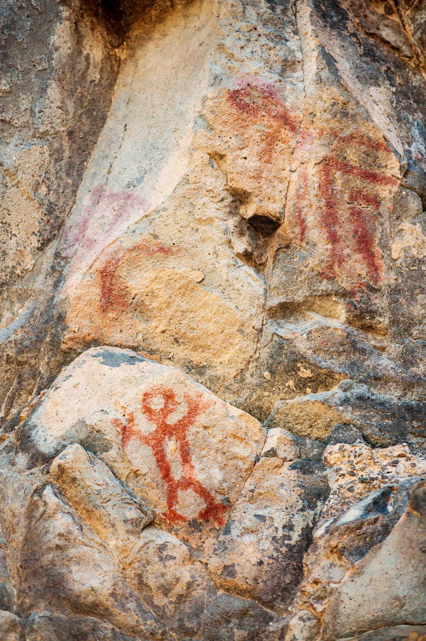Ancient rock art with red human-like figures on a stone surface.