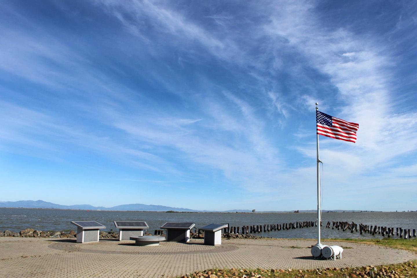 Oceanfront picnic area with benches and a waving U.S. flag under a blue sky at Port Chicago Naval Magazine National Memorial