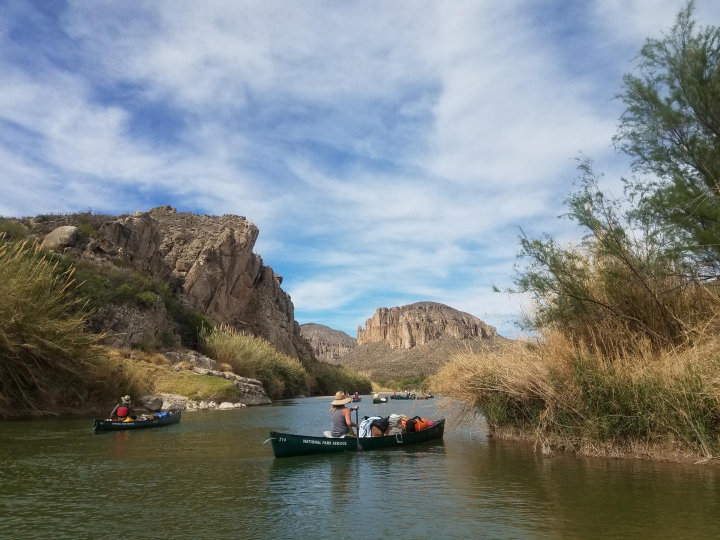 Boats on a river between rocky cliffs under a blue sky.