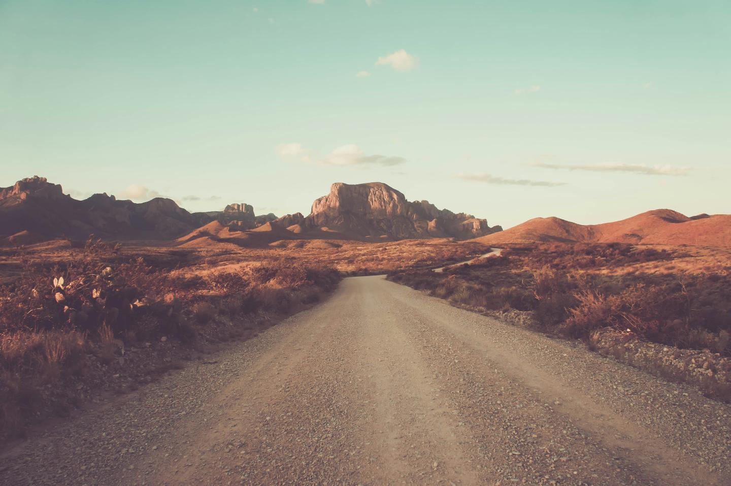 Dirt road leading to distant mountains under a clear blue sky.