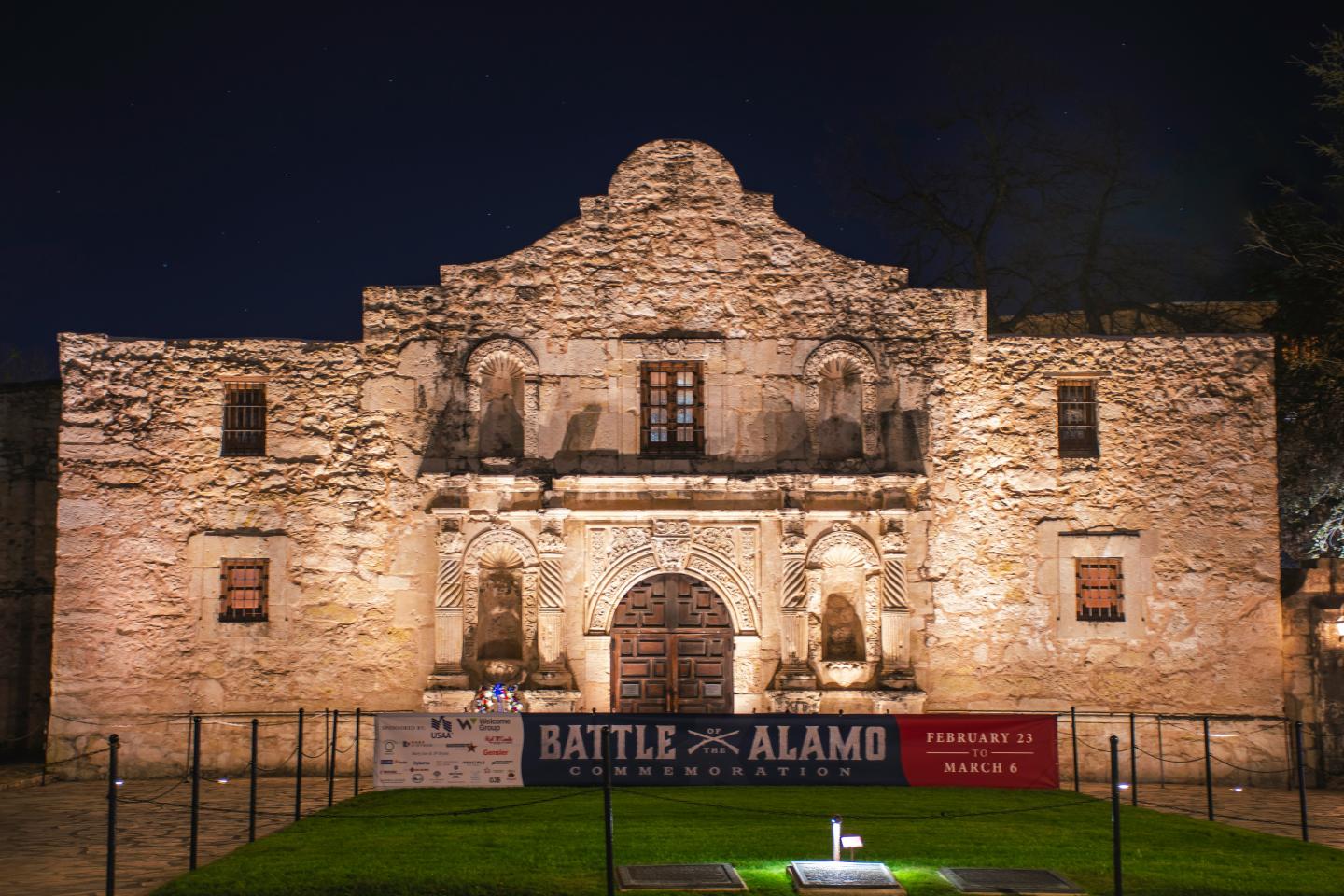 Historic Alamo building lit at night, with a banner in front.