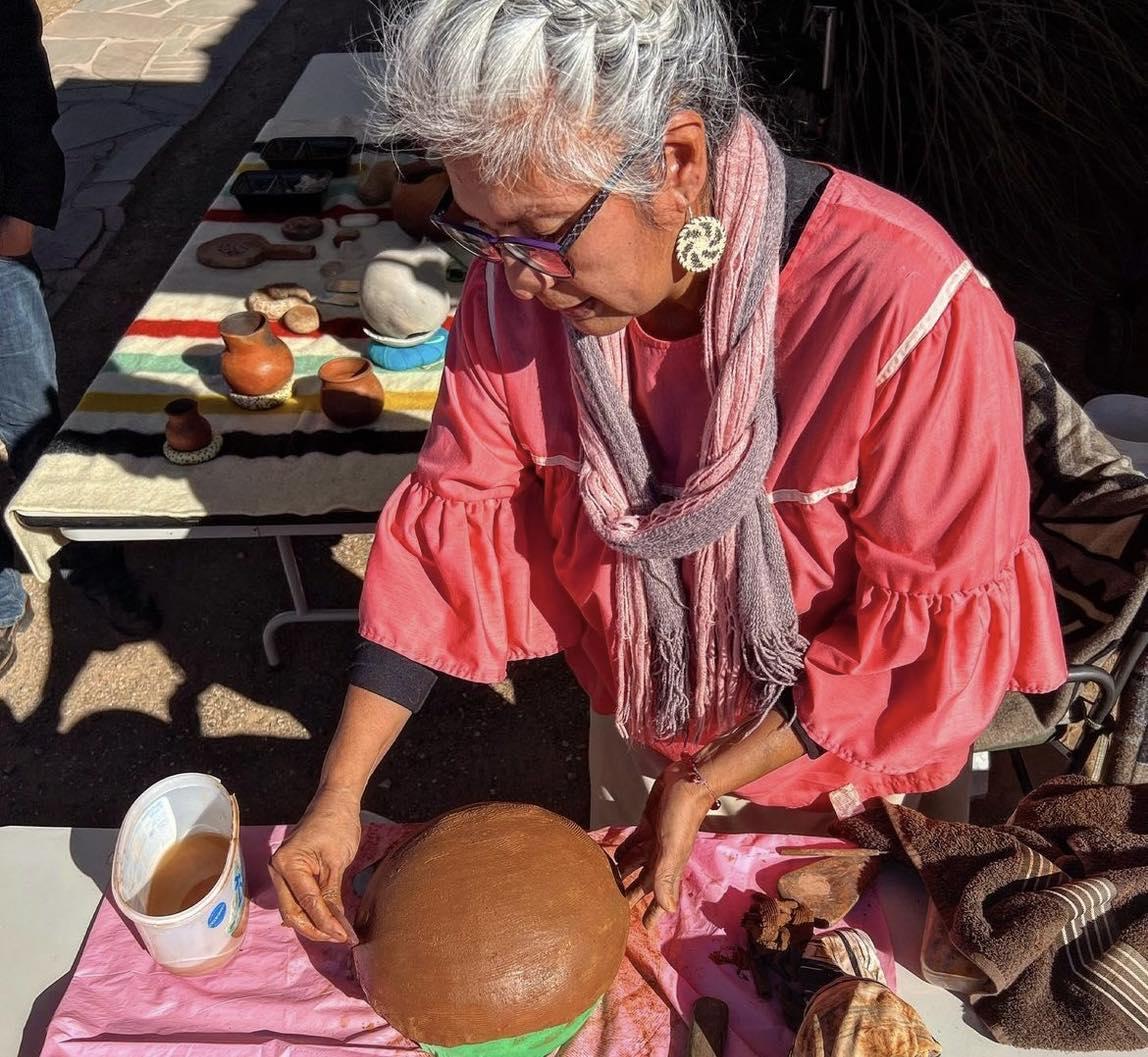 Woman in pink shirt sculpting a clay pot outdoors at Tuzigoot National Monument