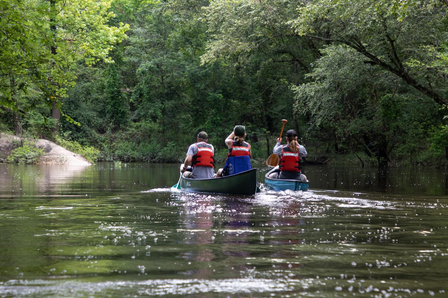 Canoes on a calm river, surrounded by dense green trees.