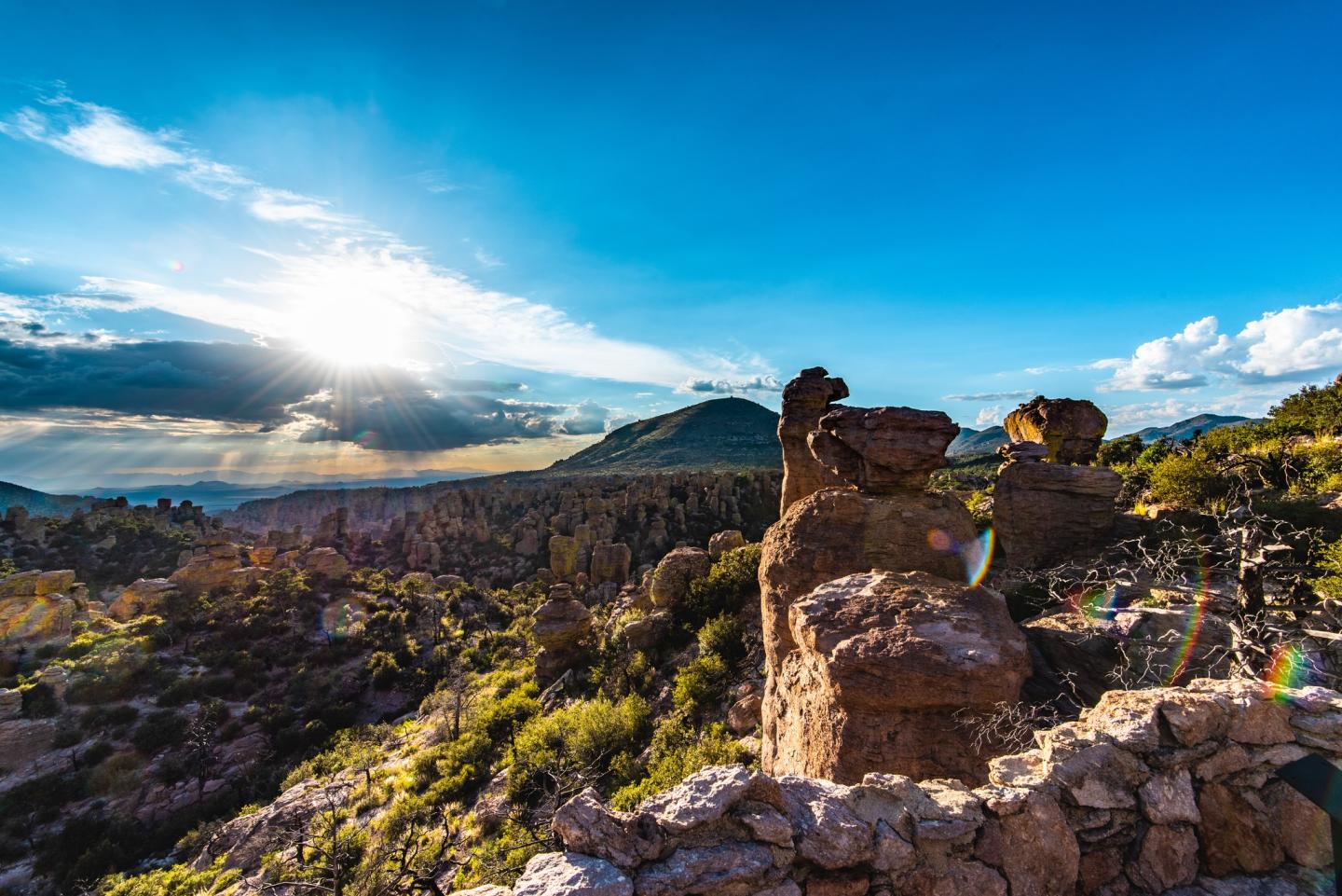 Rock formation under a bright blue sky and setting sun.