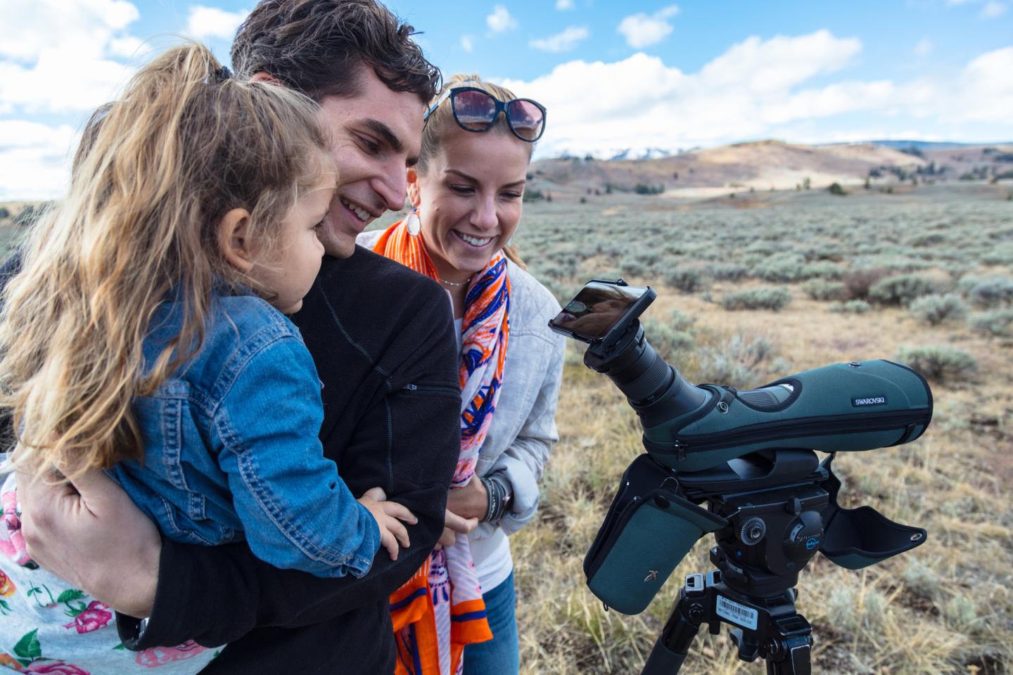Family observing nature through a spotting scope in a grassy field.