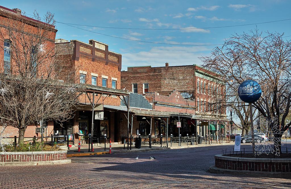Brick buildings line a quiet street next to bare trees and a blue spherical sculpture.