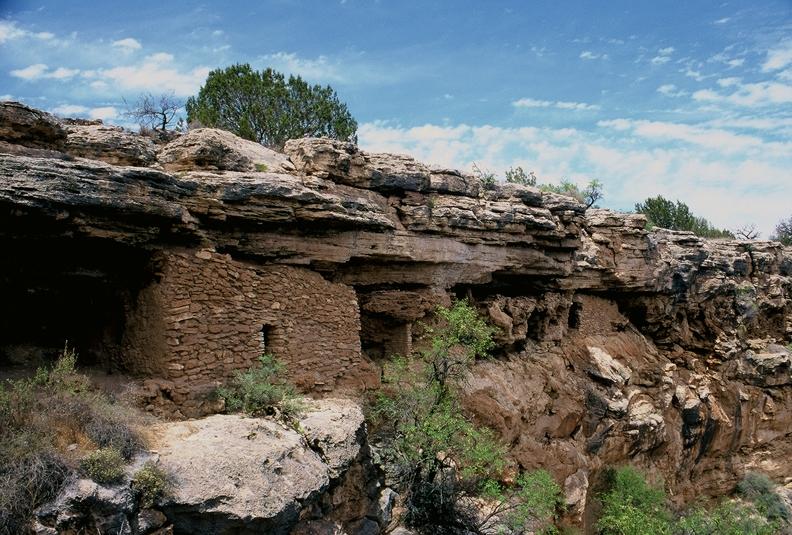 Montezuma Well liff dwelling with rocky overhang, sparse vegetation, and a blue sky.