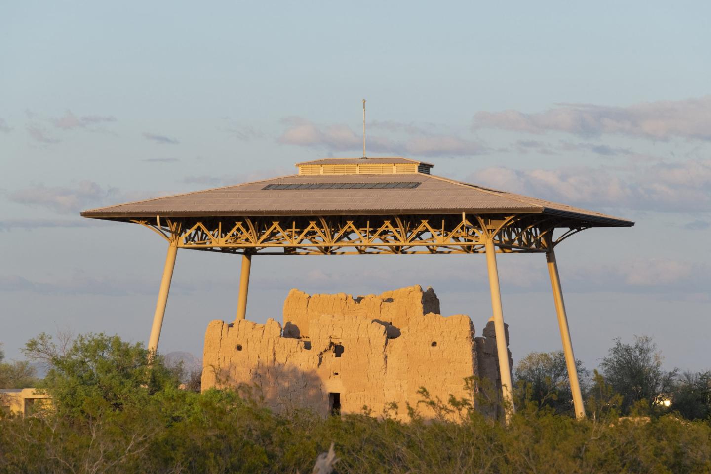 Ancient adobe ruins under a large protective canopy.