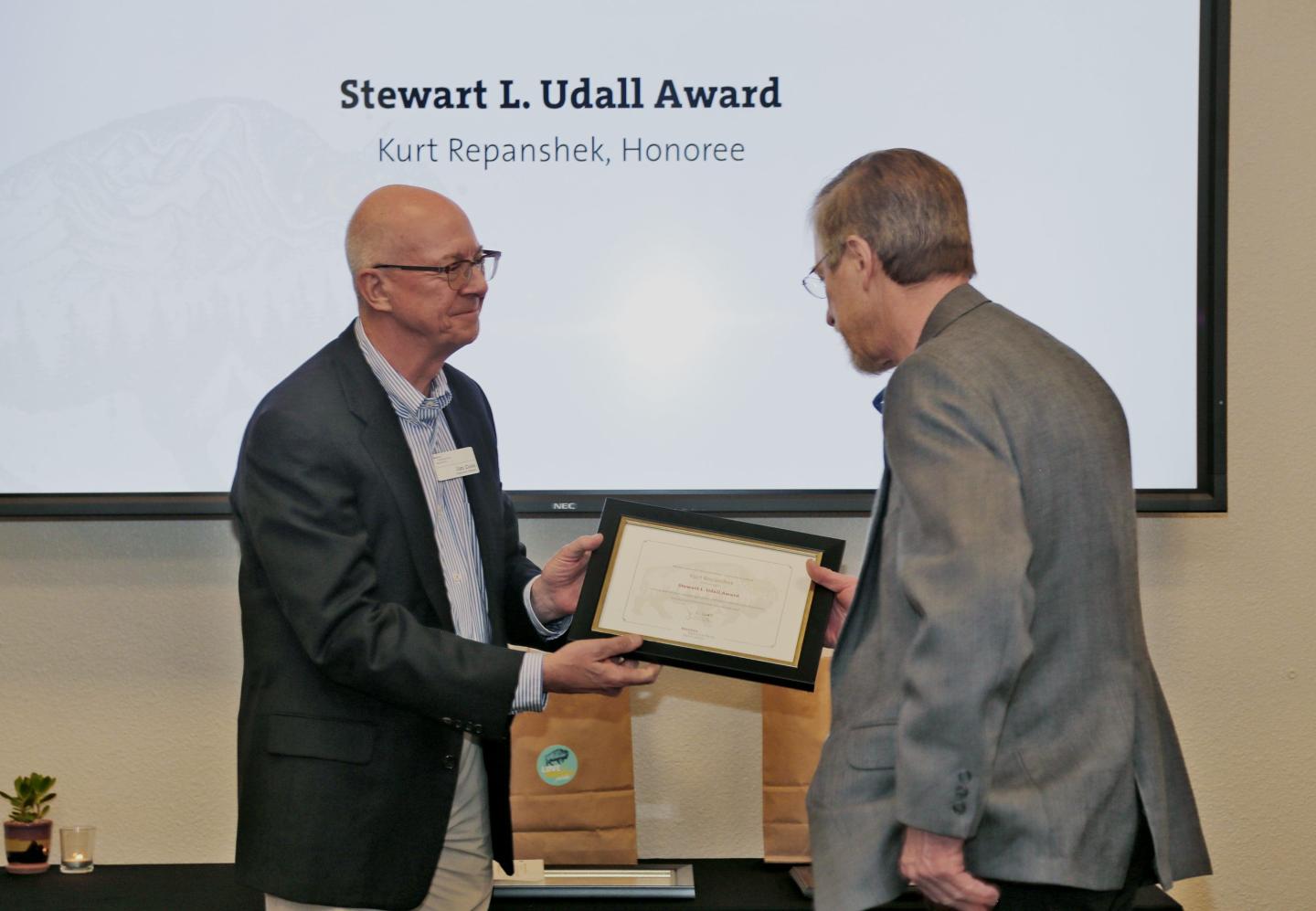 Two men exchanging a framed award at a ceremony.