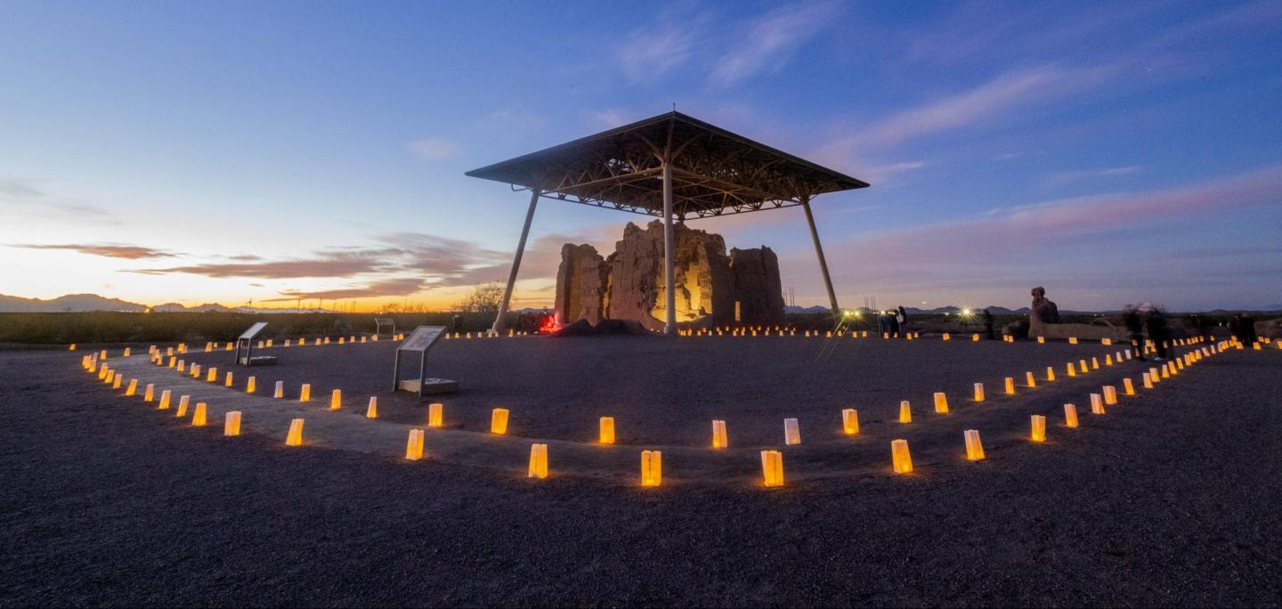 Glowing lanterns surround ruins under a canopy at sunset.