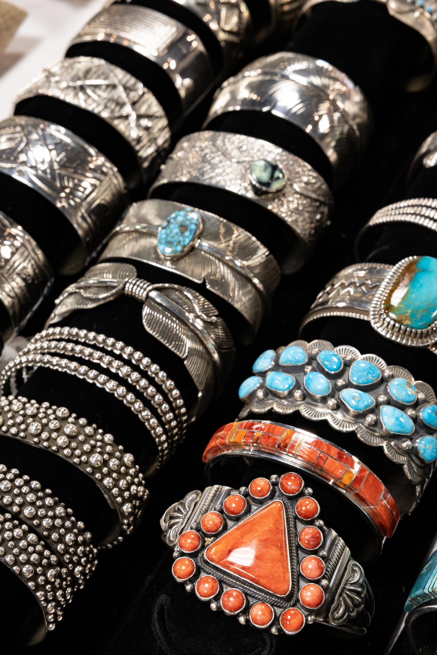 Silver, coral, and turquoise bracelets on display with intricate designs.