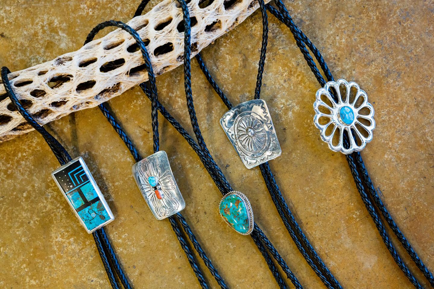 Native American bolo ties with turquoise and silver designs on a textured surface.
