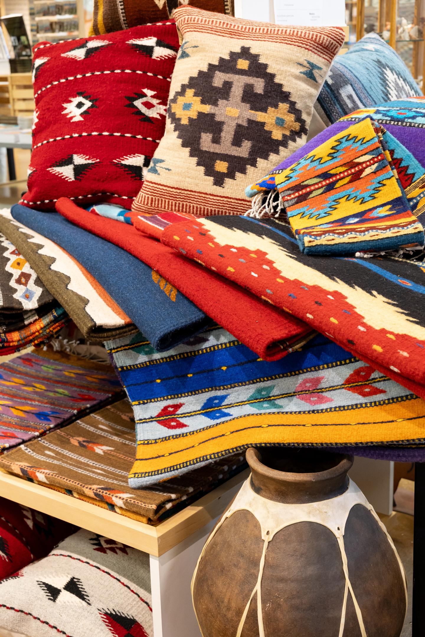 Colorful Zapotec patterned textiles and pillows stacked on a table.