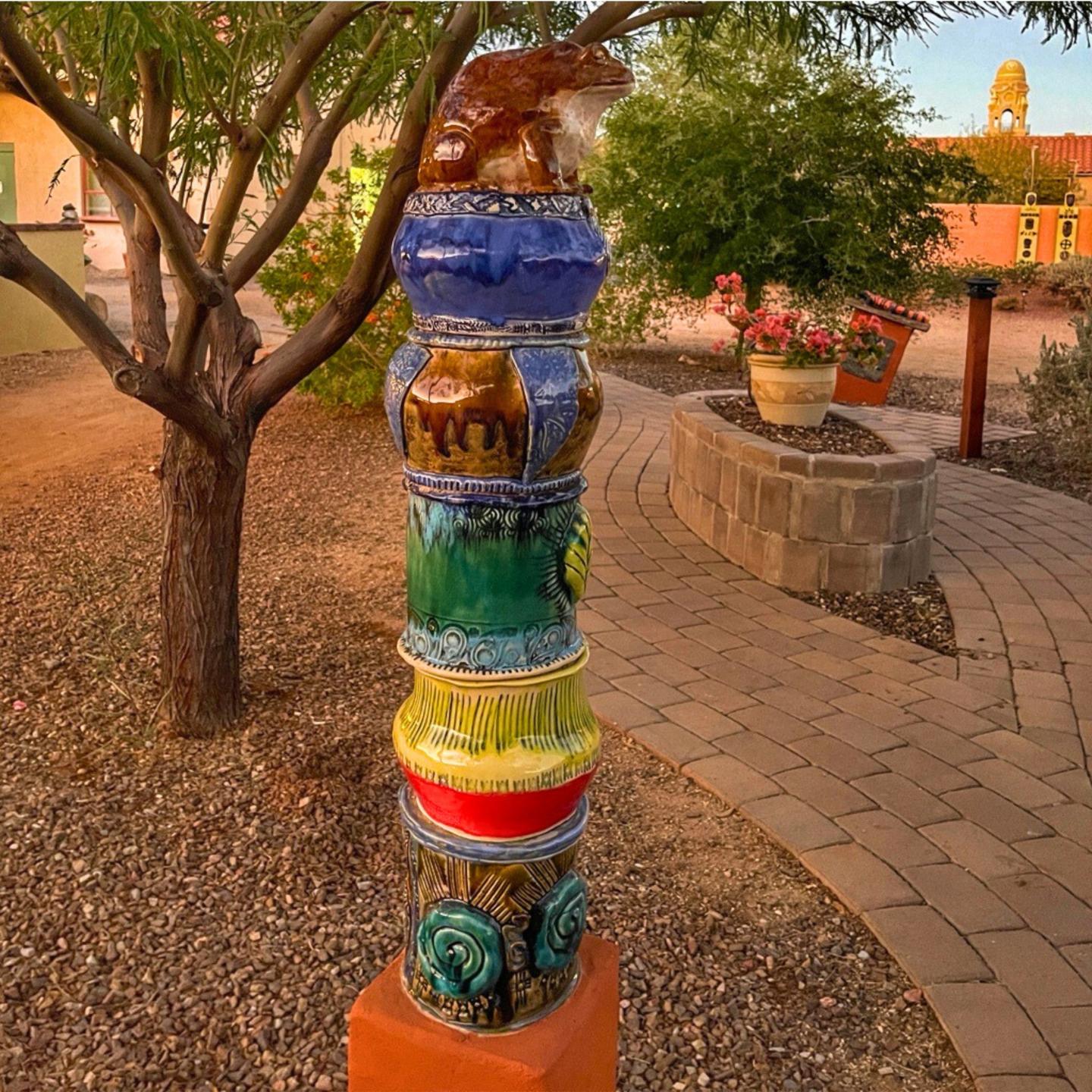 Colorful ceramic totem in a garden setting at sunset.