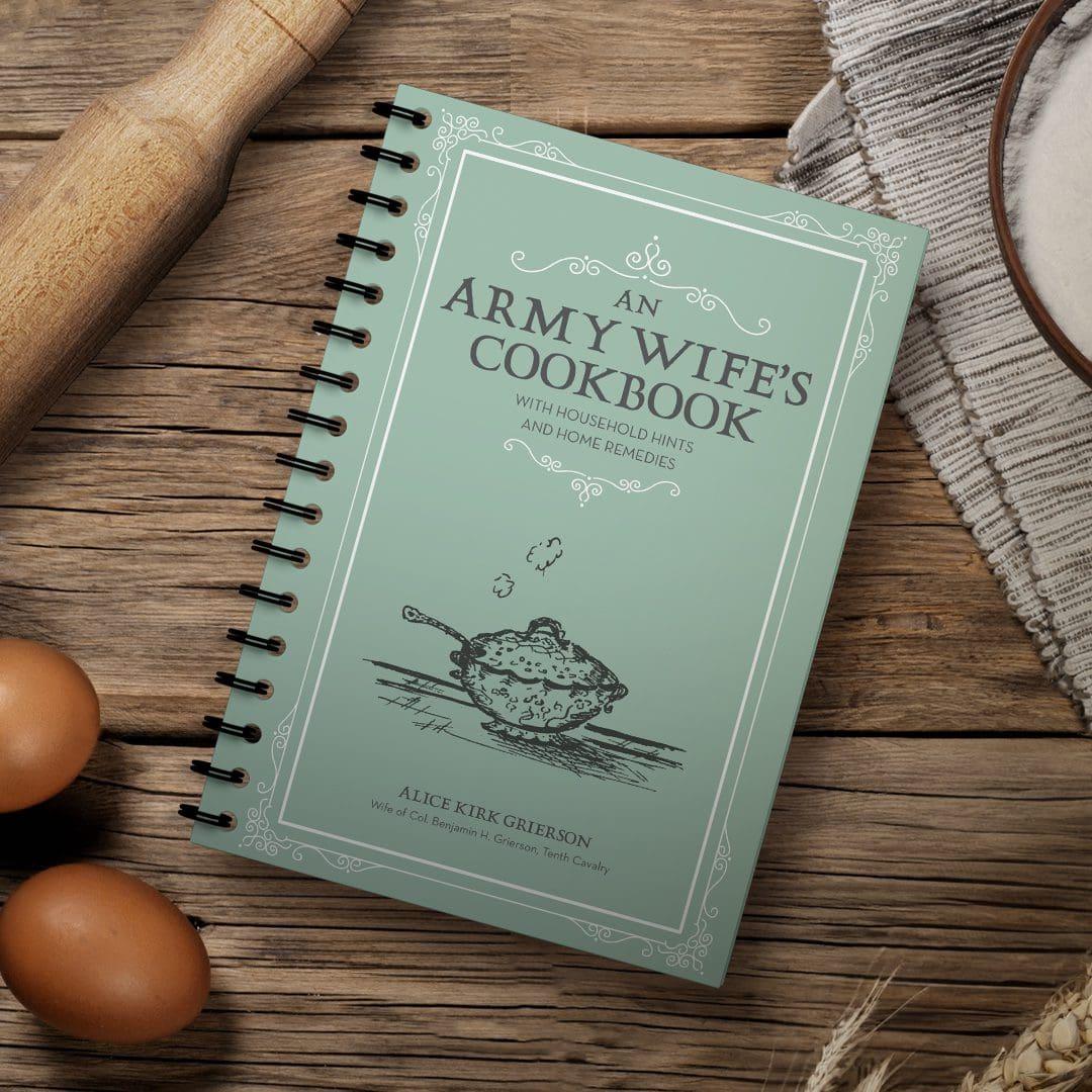 Cookbook on wooden table with eggs and rolling pin nearby.