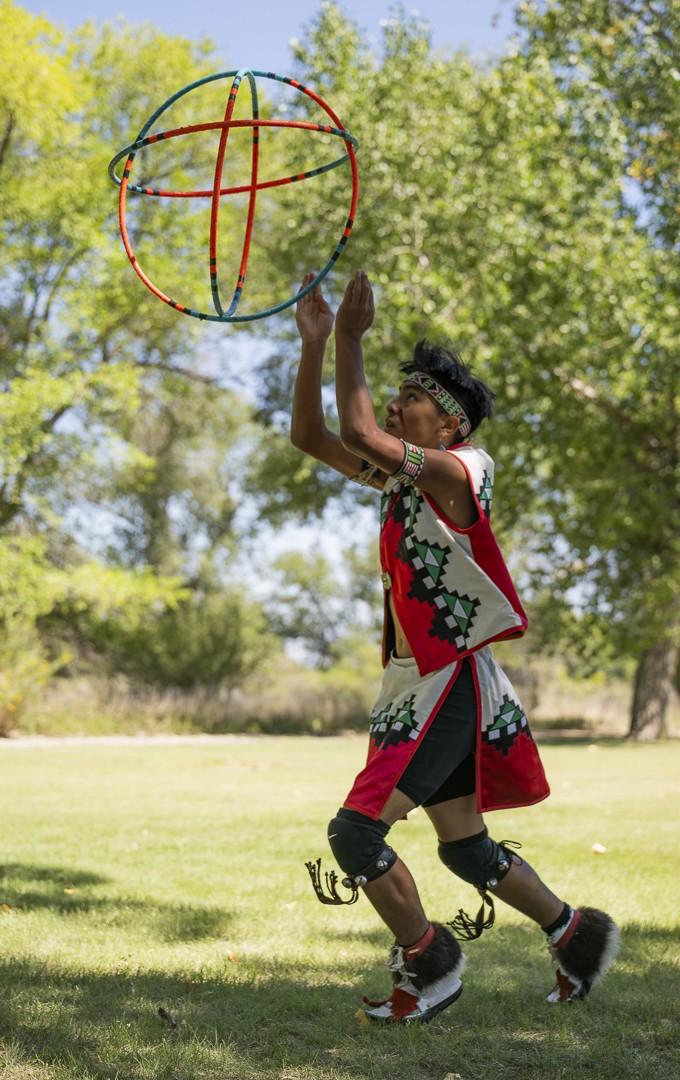 Child performs traditional dance with hoop in a park setting.