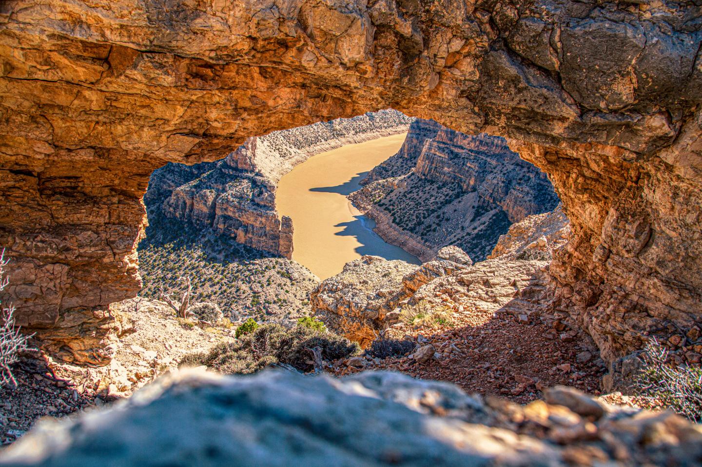 Rock arch frames a winding canyon river in vivid sunset colors.