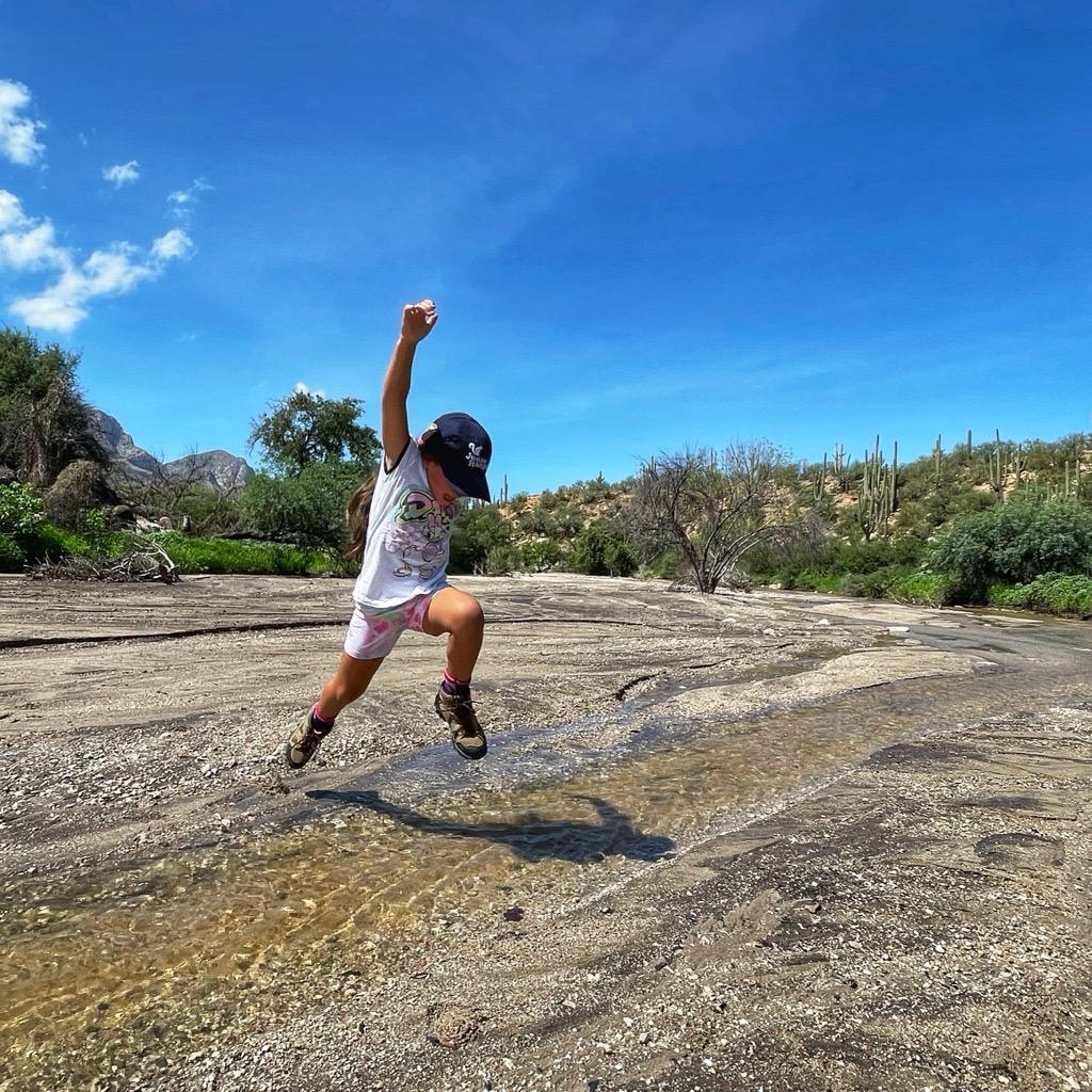 Child jumping on rocky terrain under bright blue sky.