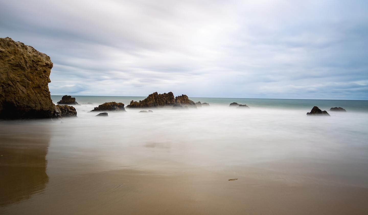 Smooth rocks on a calm beach under a cloudy sky.