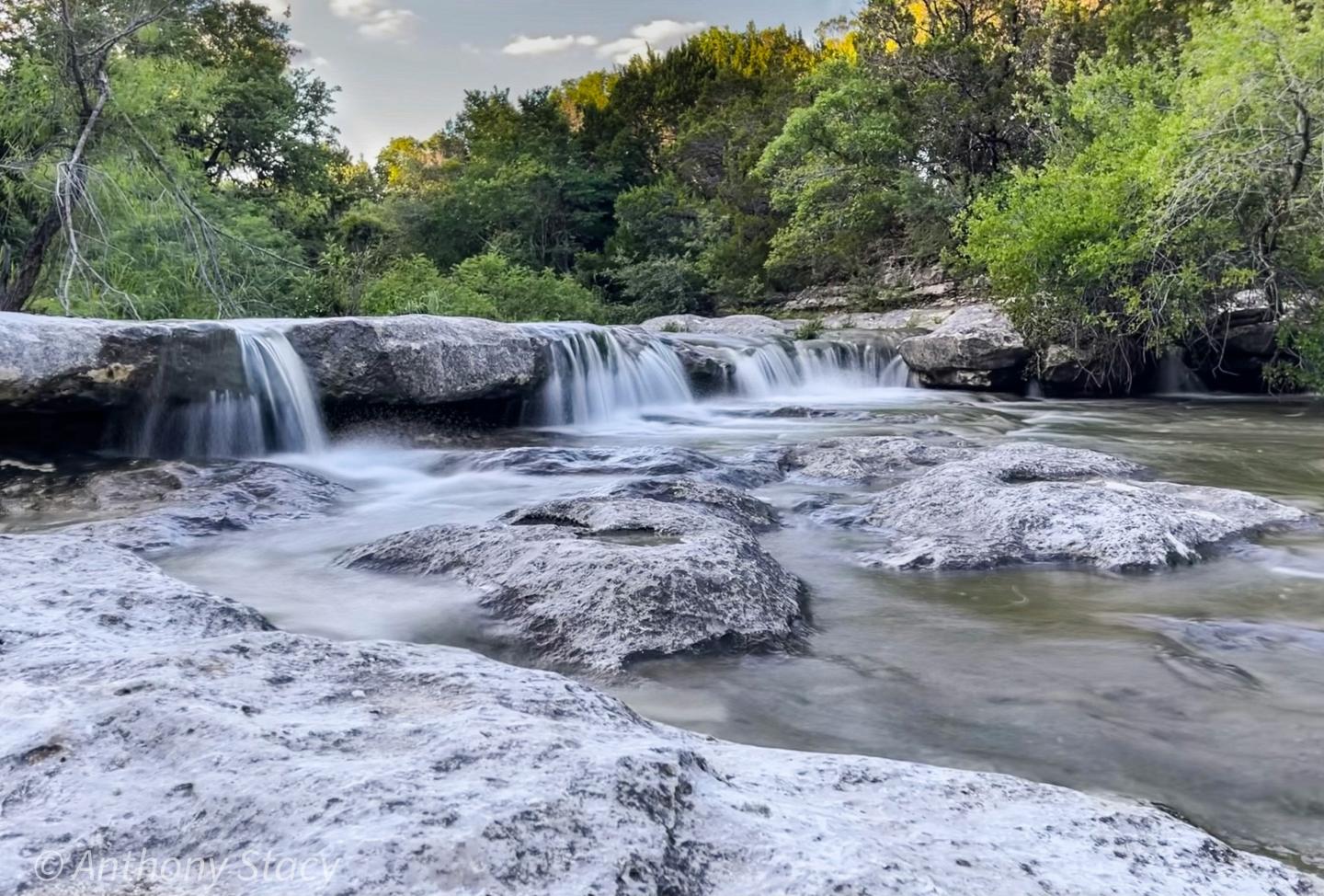Waterfall over rocks with lush green trees in the background.