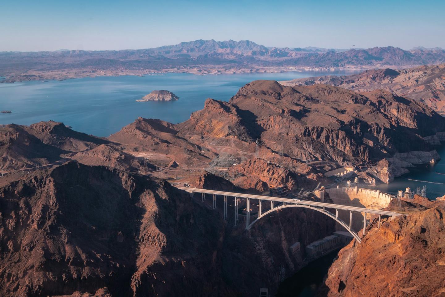 Desert landscape with a bridge crossing a canyon and a distant lake.