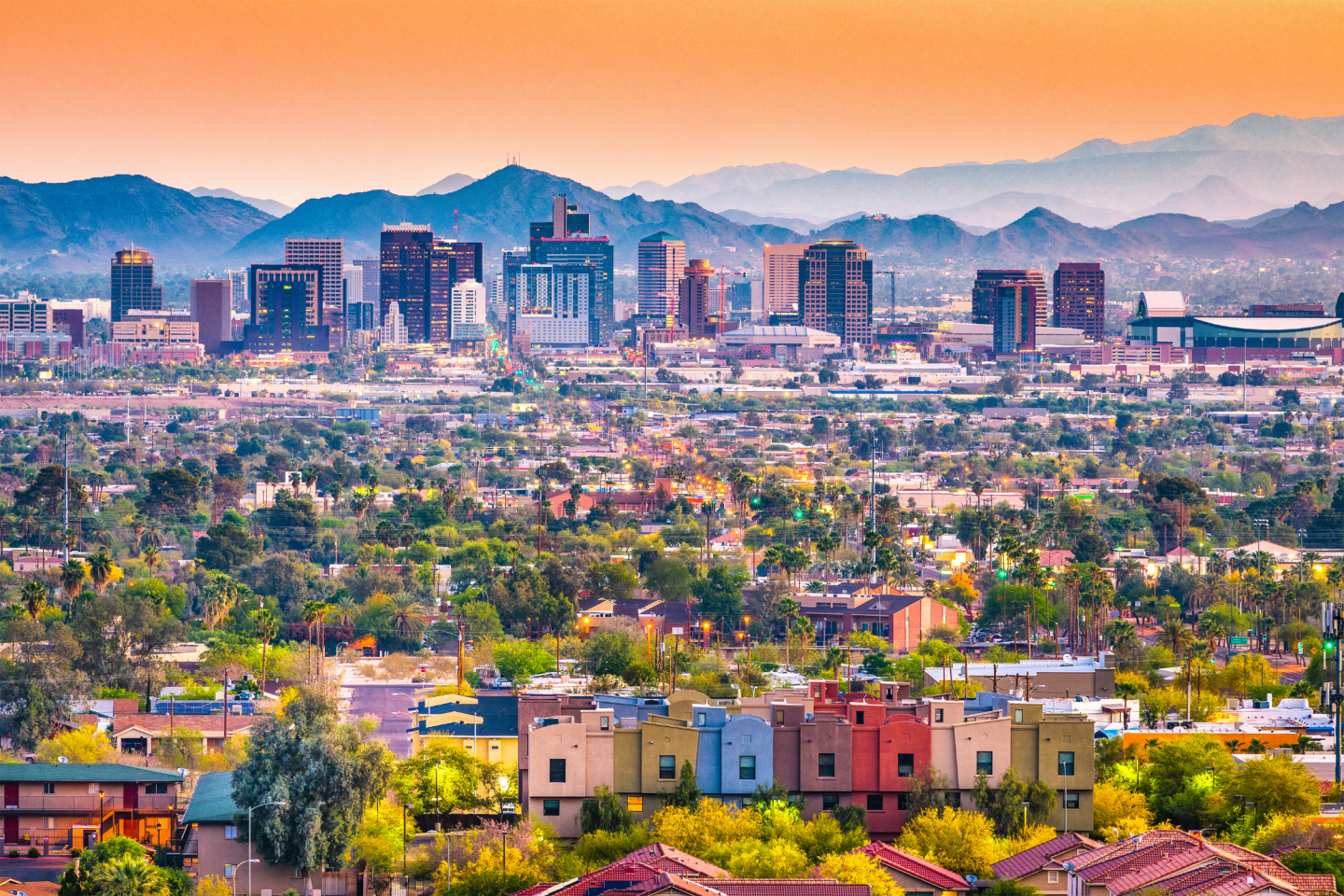 Urban skyline at sunset with mountains in the background, colorful foreground houses.