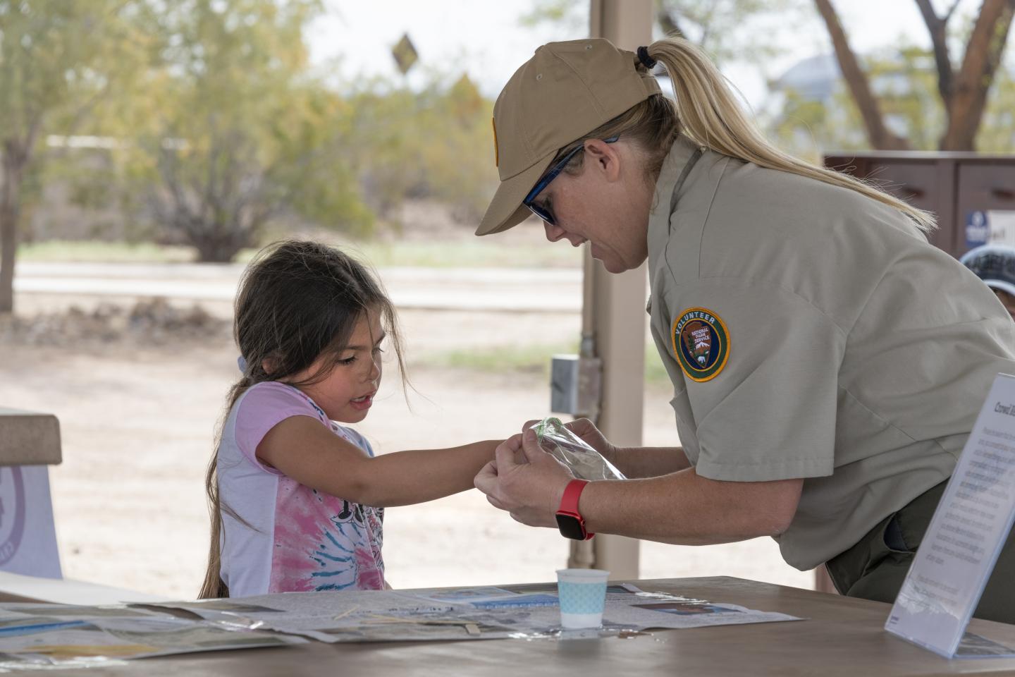 Child and park ranger at outdoor table, looking at an object.