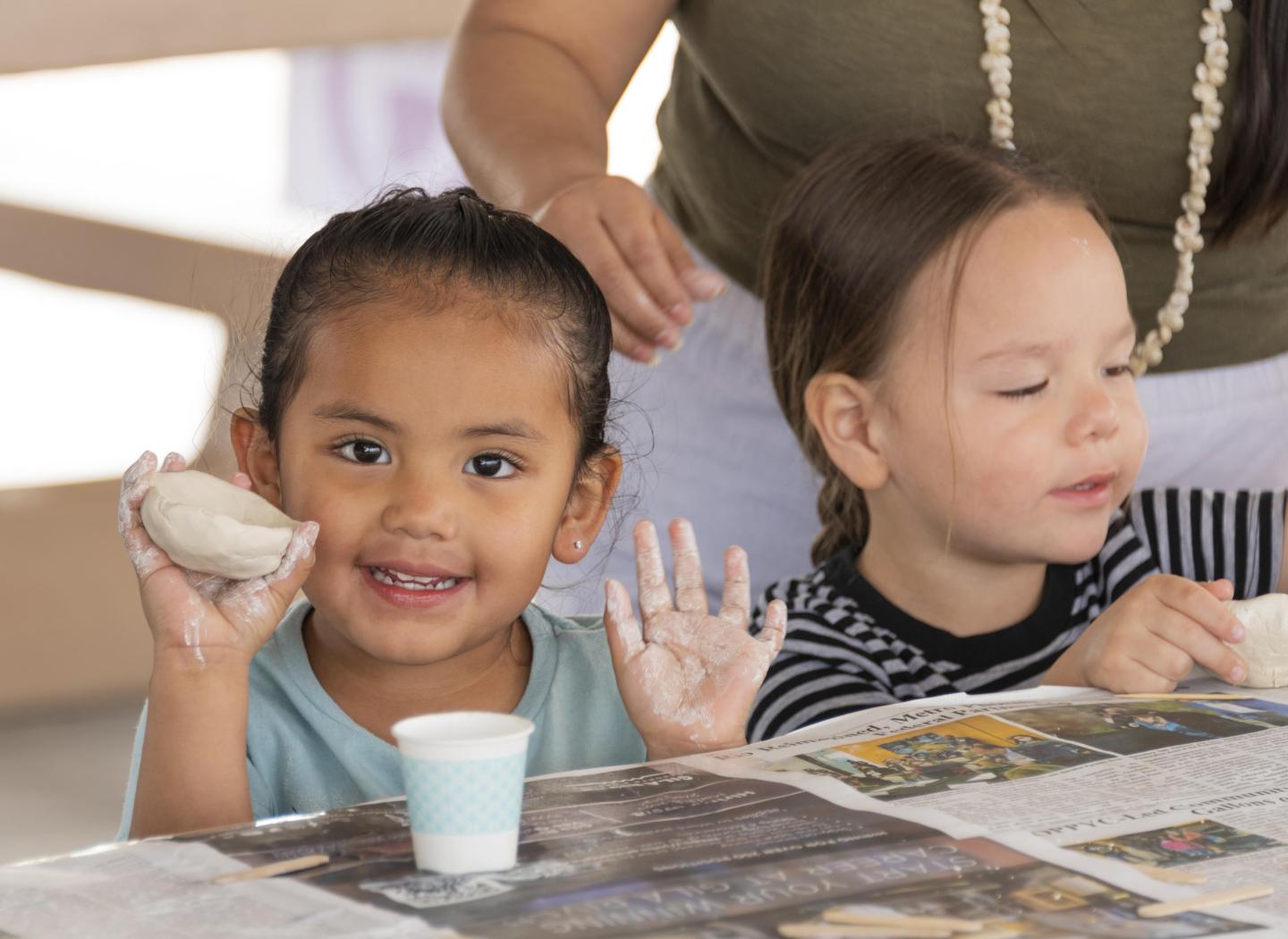 Children smiling and making pinch pots with clay at a table outside at Casa Grande Ruins.