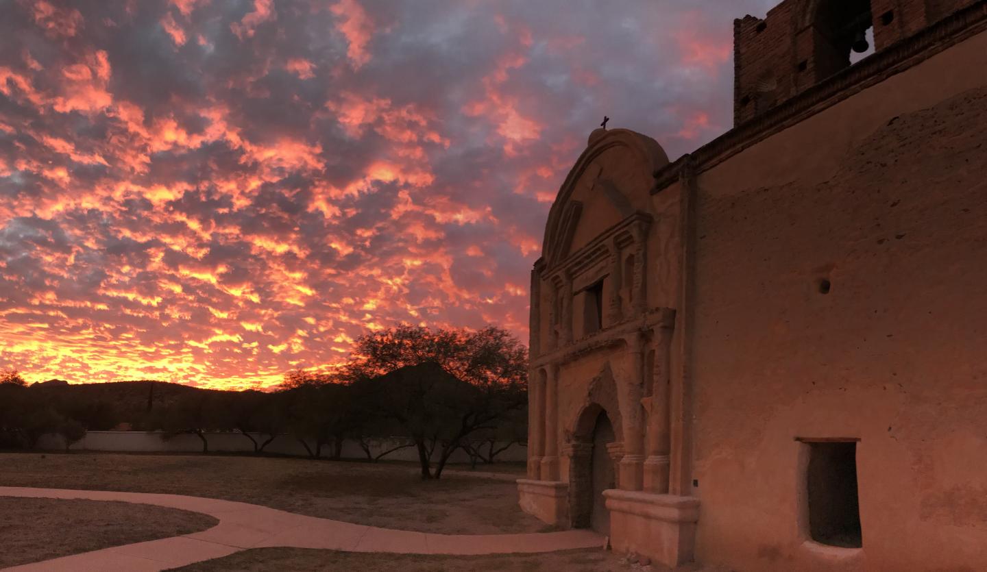 Historic mission at sunset, sky ablaze with pink and orange clouds.