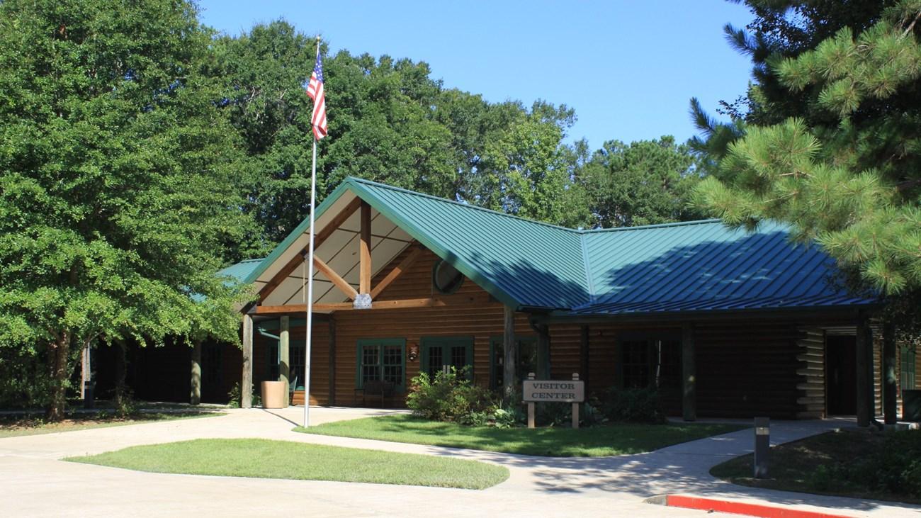 Log cabin with green roof, surrounded by trees, under clear blue sky.