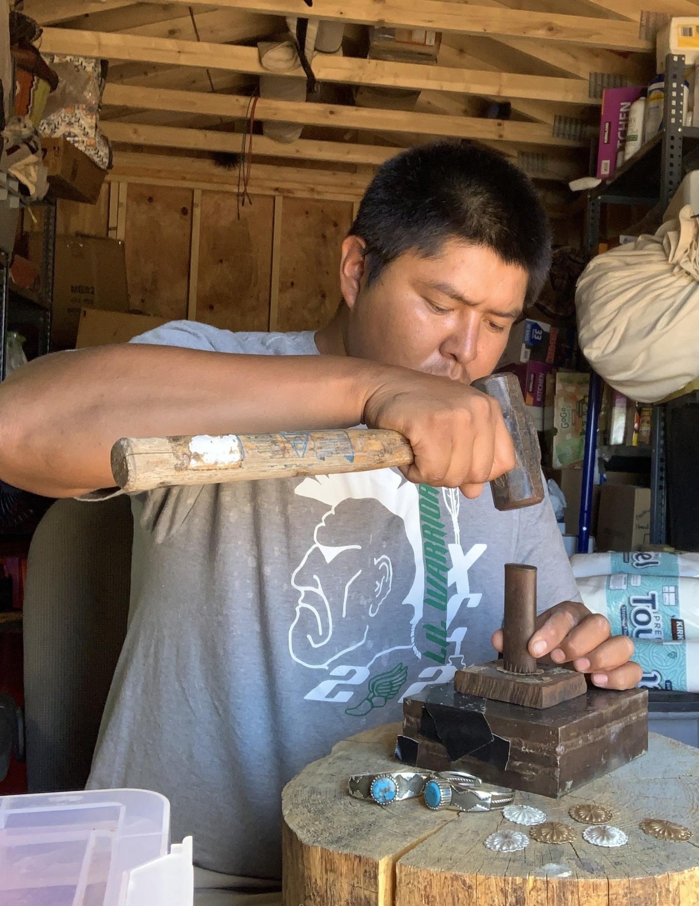 Man crafting jewelry with a hammer in a workshop.