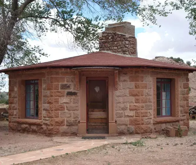 Stone hogan with red roof and chimney, surrounded by trees.