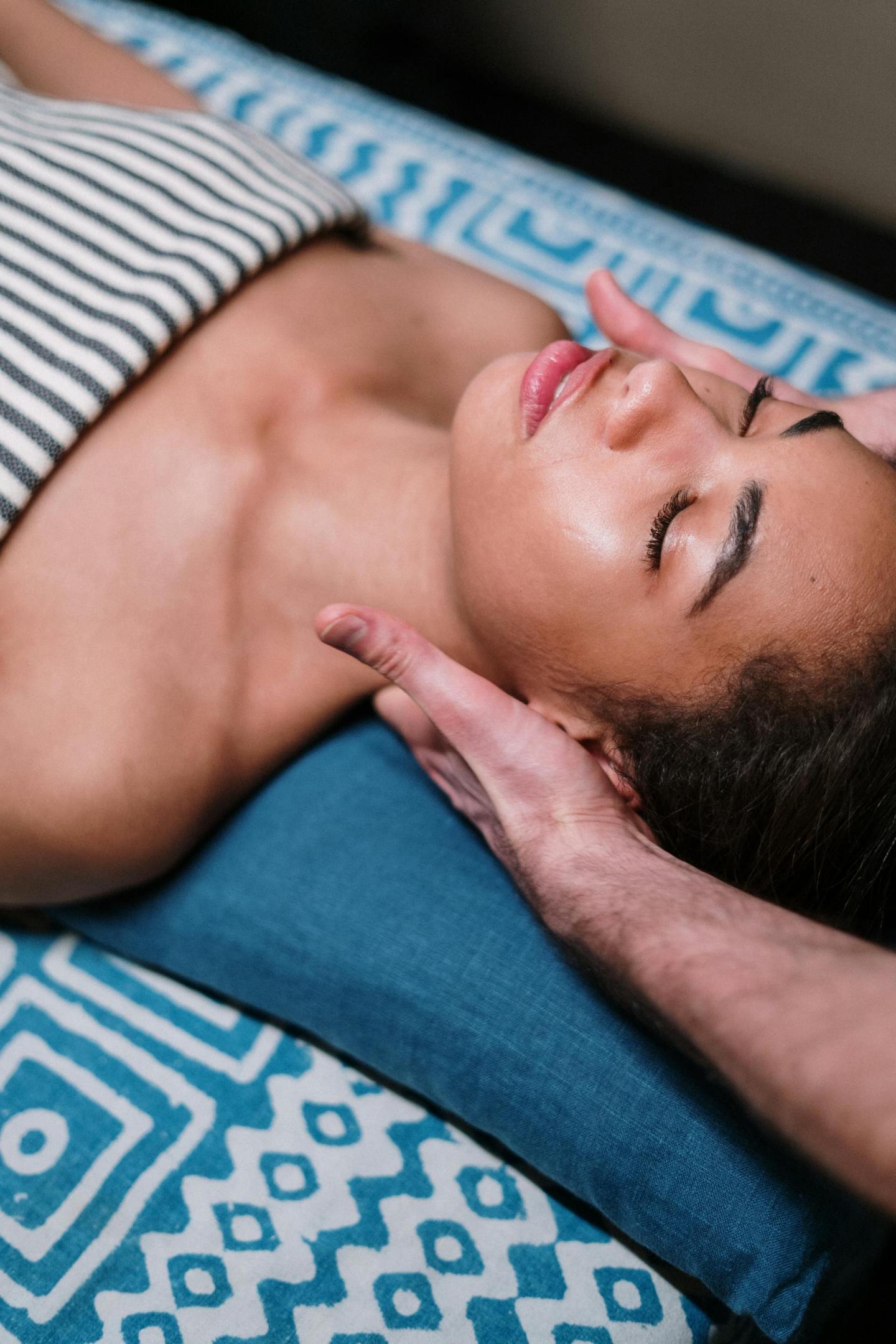 Receiving a neck massage on a striped bed, eyes closed, relaxed.